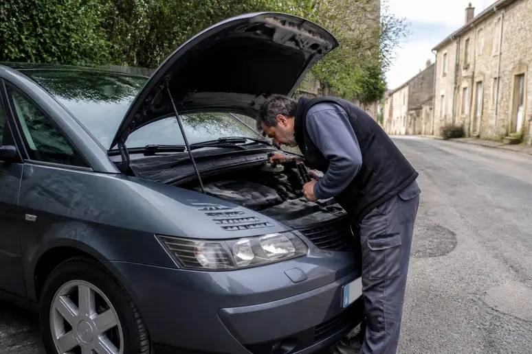 Un homme d'âge mûr inspecte le moteur d'une Renault Avantime, attentif aux détails mécaniques pour éviter les pièges de l'avantime-car.