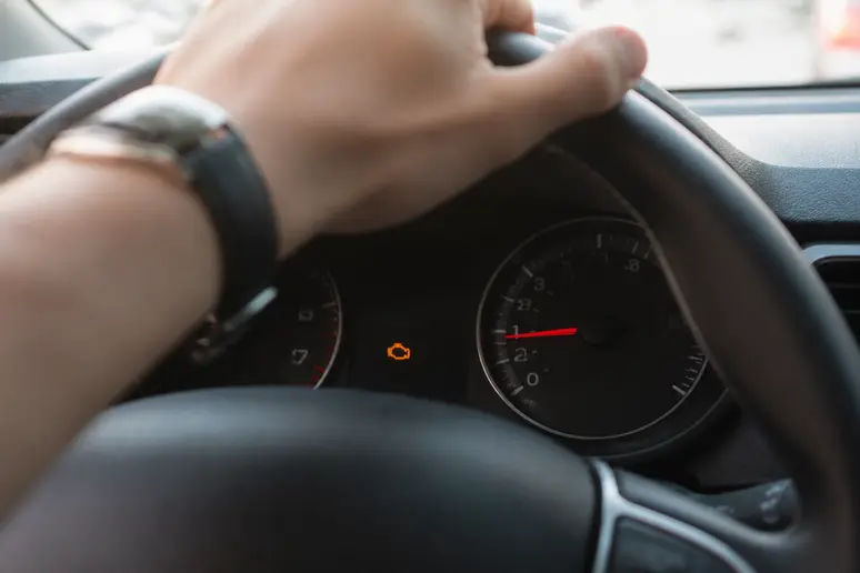 Tableau de bord d'une voiture affichant un voyant moteur orange, signalant un diagnostic urgent.