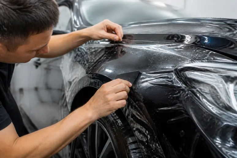 Pose minutieuse d'un film PPF transparent sur la carrosserie d'une voiture en atelier