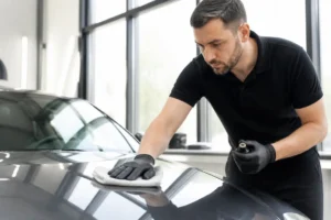 Technicien appliquant un traitement de protection céramique voiture sur la carrosserie brillante d'un véhicule dans un atelier
