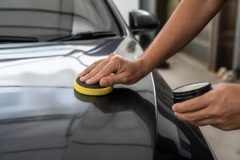Application d'une cire voiture synthétique avec un pad microfibre sur une carrosserie foncée
