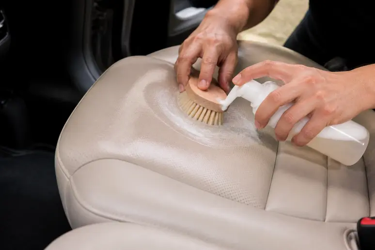 Nettoyage minutieux des sièges en cuir de voiture avec une brosse à poils souples et un mousseur.