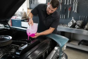 Mécanicien versant du liquide de refroidissement rose dans le radiateur d'une voiture en atelier.