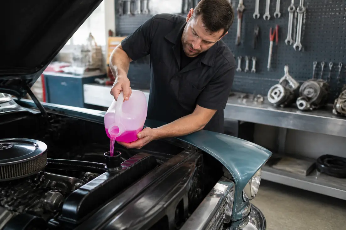 Mécanicien versant du liquide de refroidissement rose dans le radiateur d'une voiture en atelier.