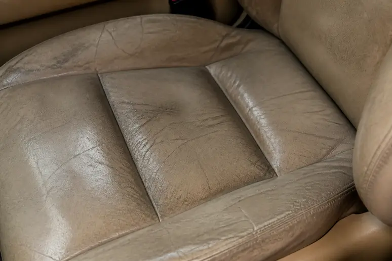 Siège conducteur en cuir sec présentant des signes d'usure et des micro-craquelures sur l'assise.