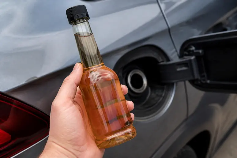 Flacon de nettoyant injecteur essence compact tenu près de la goulotte d'un réservoir automobile