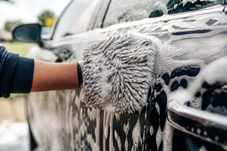 Mains gantées appliquant un shampoing voiture moussant sur la carrosserie