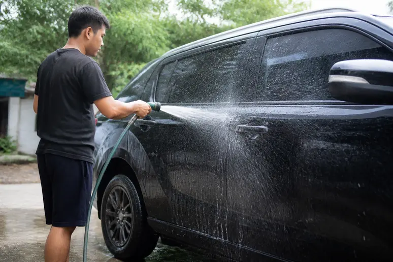 Rinçage minutieux de la carrosserie après l'application du shampoing voiture