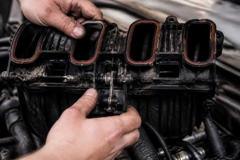 Mains d'un mécanicien inspectant le collecteur d'admission d'un moteur BMW M57 dans un atelier.