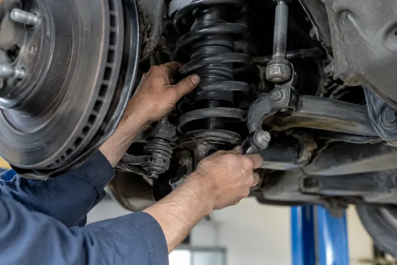 Mains d'un mécanicien inspectant la zone d'une coupelle d'amortisseur dans un garage automobile.