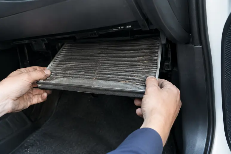 Mains d'un mécanicien retirant un filtre d'habitacle usagé de la boîte à gants d'une voiture