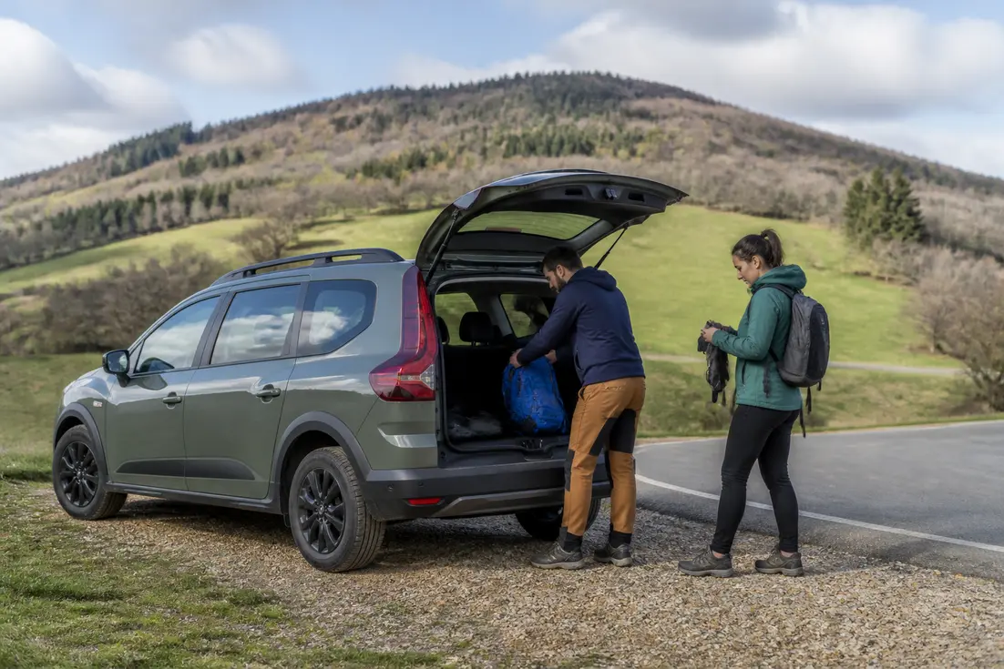 Un couple prépare son matériel de randonnée près d'un véhicule dacia-sandman-vrai-ou-faux-camping-car en pleine nature.