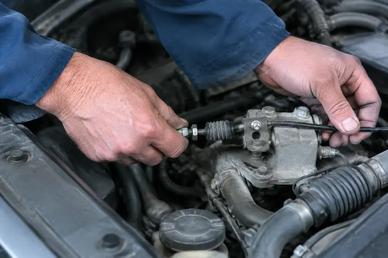 Mains d'un mécanicien ajustant le câble d'une commande d'embrayage dans un garage lumineux.