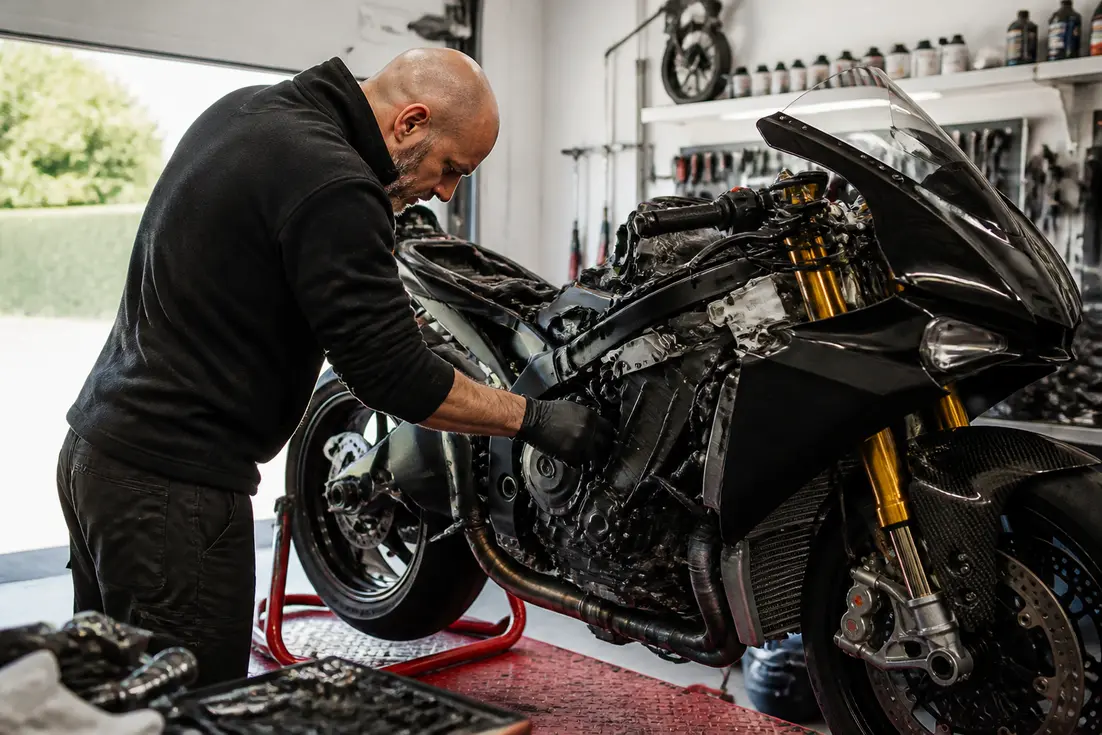 Mécanicien inspectant le moteur d'une superbike dans un atelier pour identifier la-plus-rapide-moto-du-monde.