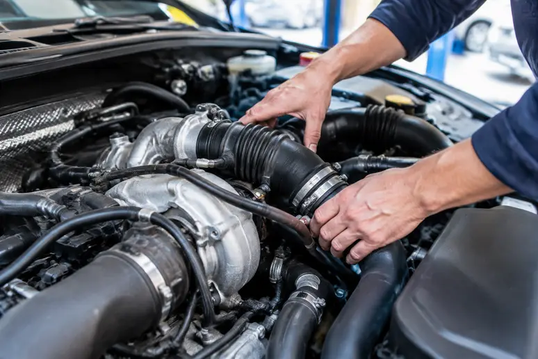 Mains d'un mécanicien inspectant le circuit d'air et les durites sous le capot d'une voiture.