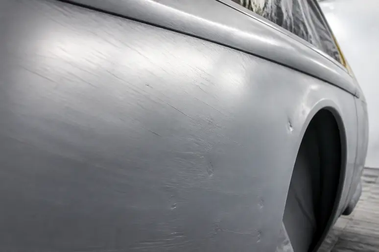 Défauts de ponçage visibles et micro-rayures sur une tôle de voiture mal préparée