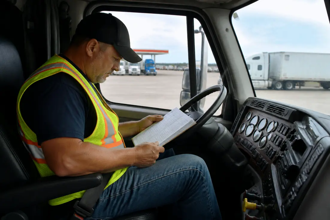 Un chauffeur routier consulte son tableau-temps-de-conduite-et-de-repos lors d'une pause obligatoire dans la cabine de son camion