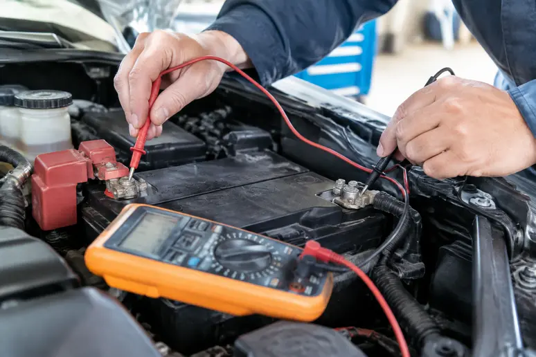 Multimètre branché aux bornes d'une batterie automobile pour tester alternateur.