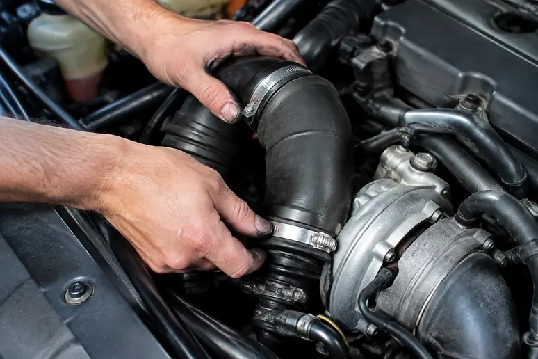 Mains d'un mécanicien inspectant les durites et les colliers de serrage dans le compartiment moteur.